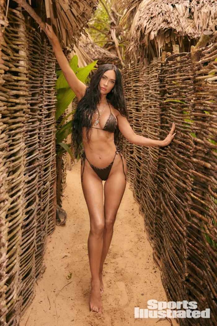 Megan Fox stands between wooden walls and poses in a brown leather bikini.